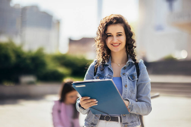 Estudiante de pie con su cuaderno de notas mientras sus amigos están estudiando detrás de ella - Foto, imagen