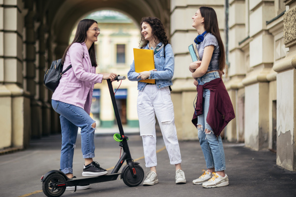 Студентка на скутере встречается со своими одноклассниками в кампусе - Фото, изображение