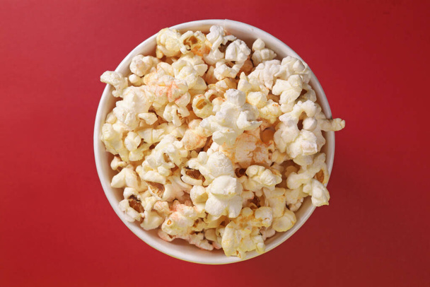 Paper cup with popcorn on red background, top view - Fotó, kép