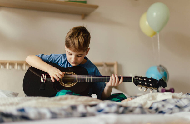Happy boy playing on the guitar in the room. - Foto, Imagem