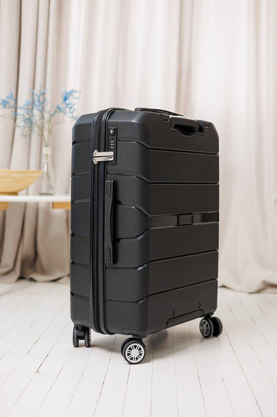 Mala forte de plástico preto para transportar bagagem em um fundo branco. Uma mala brilhante para viajar - Foto, Imagem