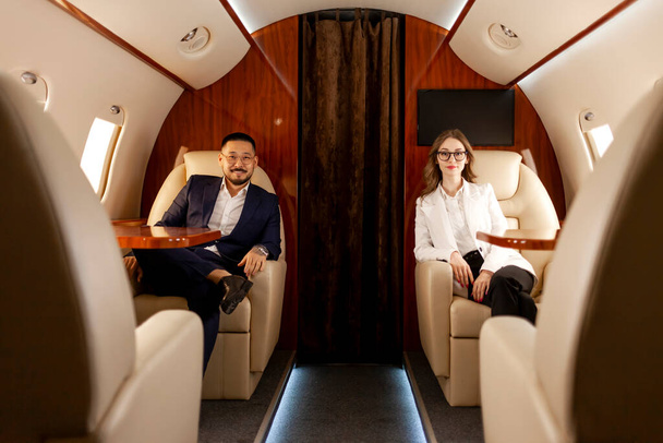 biznesmeni siedzą w prywatnym odrzutowcu i latają samolotem, odnoszący sukcesy azjatycki biznesmen z koleżanką latają pierwszą klasą - Zdjęcie, obraz