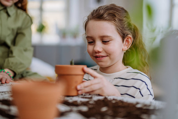 Happy little girl looking at growing plant in a ceramics pot. - Photo, image