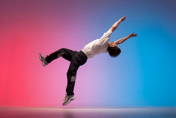 guy acrobat doing back fat in new lighting, male dancer jumps and falls in the air on red blue background, hiphop performer does trick and levitates in the air - Photo, image