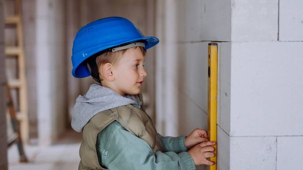 Little boy in unfinished house measuring wall in unfinished house with a spirit level. - Foto, imagen