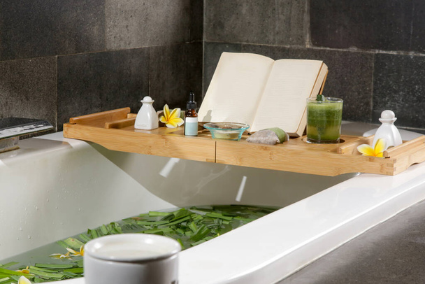 Tub vol water en kruiden met houten bad lade met diverse cosmetische producten, ontspanning en welzijn concept van levensstijl - Foto, afbeelding