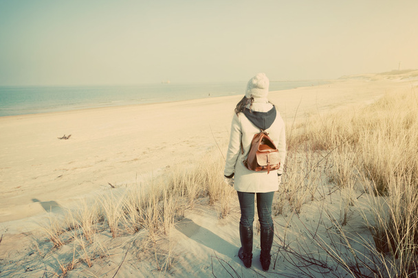 Женщина с ретро рюкзаком, смотрящая на море
 - Фото, изображение