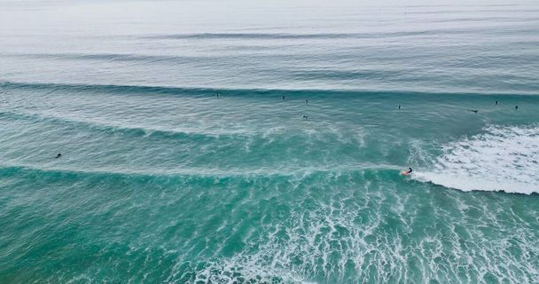 An aerial shot of people surfboarding and swimming in the calm waters of the blue ocean - 写真・画像