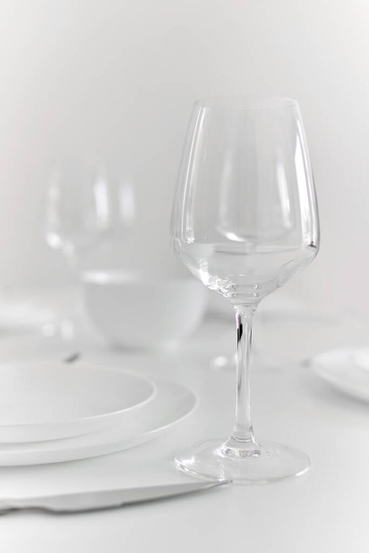 Close up view of empty wine glass on table prepared for dinner with tablecloth and plates, no people. Eating, life event celebration  - Photo, image