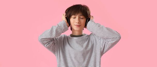 Teenage chlapec ve sluchátkách poslech hudby na růžovém pozadí - Fotografie, Obrázek