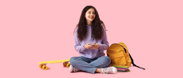 Female student with mobile phone, backpack and skateboard on pink background - Photo, image
