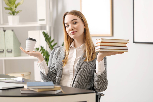 Молодая деловая женщина с чашкой кофе и книгами в офисе. Концепция баланса - Фото, изображение