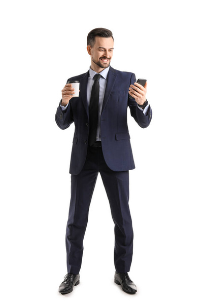 Красивый бизнесмен с чашкой кофе и мобильного телефона на белом фоне - Фото, изображение