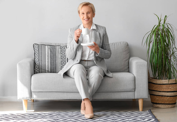 Зрелая деловая женщина пьет кофе, сидя на диване в офисе - Фото, изображение