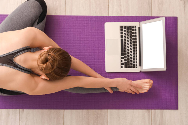 Sporty young woman with laptop doing yoga in gym, top view - Photo, Image