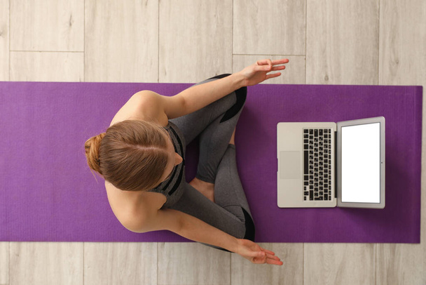Sporty young woman with laptop doing yoga in gym, top view - Fotoğraf, Görsel