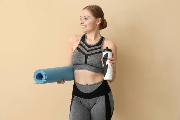 Sporty young woman with yoga mat and bottle of water on beige background - Foto, Imagem