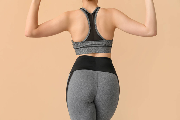 Young woman in sportswear on beige background, back view - Photo, Image