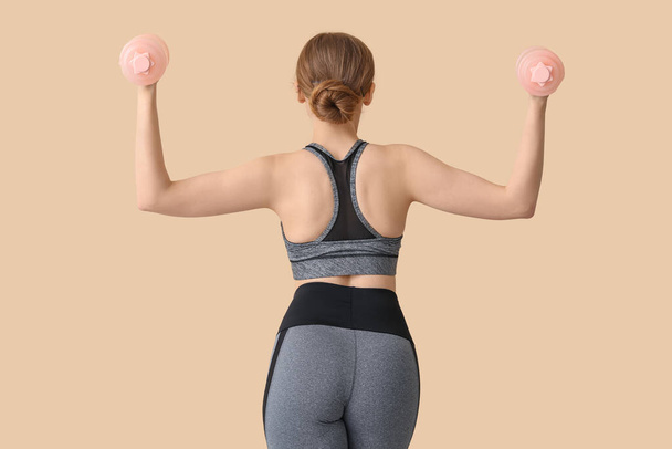 Sportos fiatal nő súlyzókkal bézs alapon - Fotó, kép