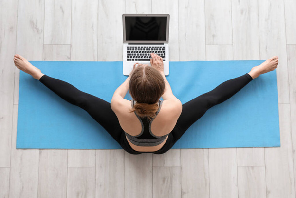 Sporty young woman with laptop doing yoga in gym, top view - Φωτογραφία, εικόνα