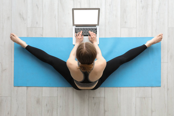 Urheilullinen nuori nainen kannettavan tietokoneen kanssa tekee joogaa kuntosalilla, ylhäältä - Valokuva, kuva