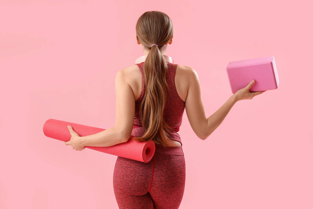Sporty young woman with mat and block for yoga on pink background - Photo, Image