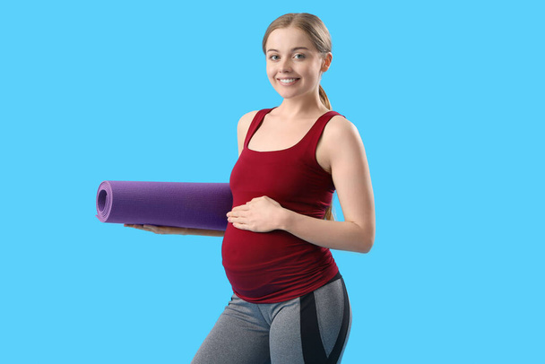 Terhes fiatal nő jóga szőnyeg kék háttér - Fotó, kép