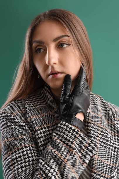 Portrait of beautiful young woman in leather gloves and coat on green background - Foto, imagen