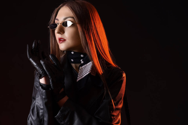 Belle jeune femme en gants de cuir et veste sur fond sombre - Photo, image