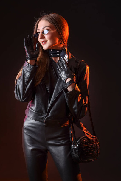 Beautiful young woman in leather gloves and jacket on dark background - Foto, imagen