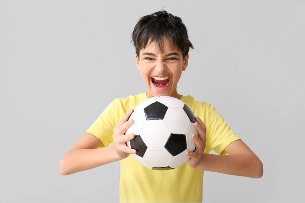 Niño agresivo con pelota de fútbol sobre fondo gris - Foto, imagen