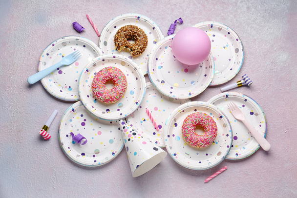 Placas descartáveis de papel com donuts, chapéu de festa, sopradores e velas no fundo grunge - Foto, Imagem