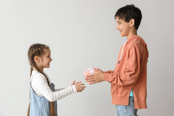 Niño saludando a su hermana con un regalo sobre fondo claro. Celebración del Día de los Niños - Foto, imagen