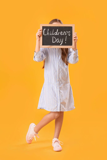 Niña sosteniendo pizarra con texto DÍA DE LOS NIÑOS sobre fondo amarillo - Foto, Imagen
