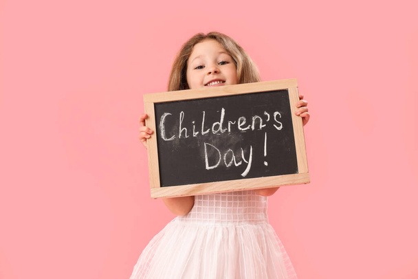 Little girl holding chalkboard with text CHILDREN'S DAY on pink background - Фото, изображение