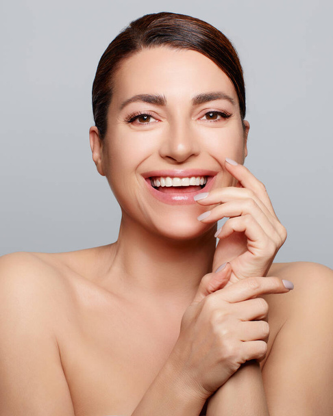 Beauty and Skincare Concept. Smiling natural woman face with nude makeup on a flawless skin. Studio portrait on grey background - Foto, afbeelding