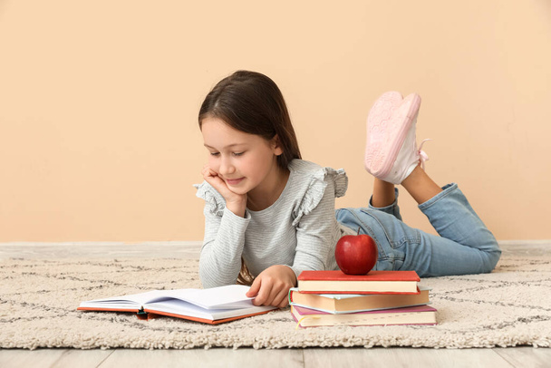 Little girl reading book near beige wall. Children's Day celebration - Фото, изображение