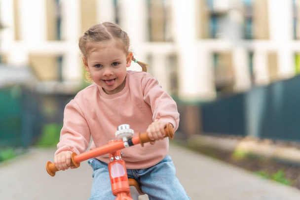 Mała dziewczynka na rowerze biegowym na dziedzińcu rezydencji w Pradze, Europa. Wysokiej jakości zdjęcie - Zdjęcie, obraz