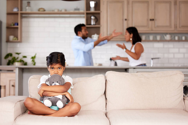 Una niña asustada sosteniendo un peluche en una casa abusiva. Pareja joven luchando mientras su hijo se sienta en el sofá. - Foto, Imagen