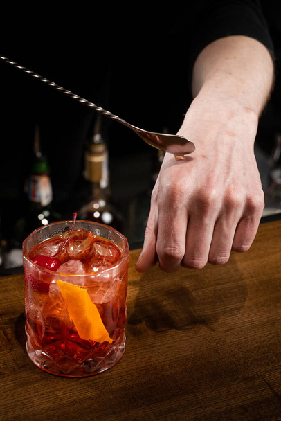 Bartender puts a drop of Negroni alcoholic cocktail on his hand and tastes it. Barman prepares classical Negroni cocktail at the bar - Photo, Image