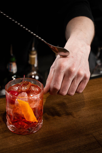 Ο μπάρμαν βάζει μια σταγόνα αλκοολούχο κοκτέιλ Νεγκρόνι στο χέρι του και το δοκιμάζει. Barman ετοιμάζει κλασικό κοκτέιλ Negroni στο μπαρ - Φωτογραφία, εικόνα
