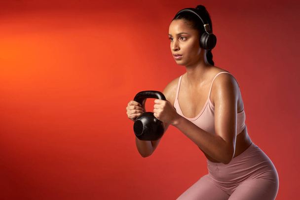 Розчавити її тренування. Студійний знімок спортивної молодої жінки робить присідання чайника на червоному тлі
 - Фото, зображення
