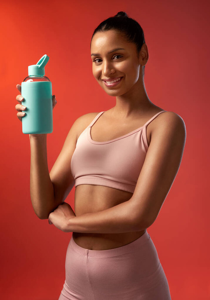 Water is key when working out. Studio portrait of a sporty young woman holding a water bottle against a red background - Photo, Image