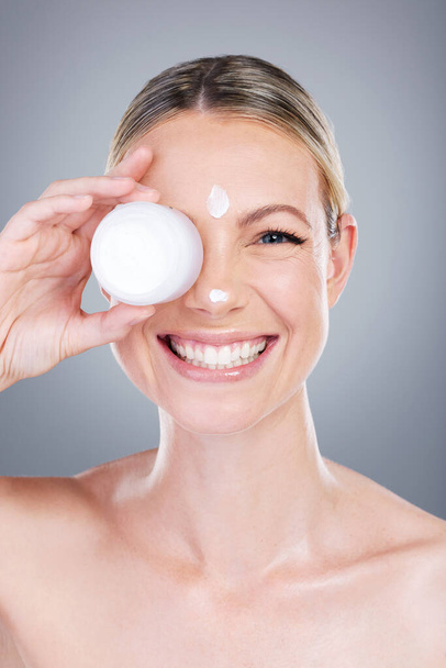 Lotion seals moisture into the skin for a glowing look. Studio portrait of an attractive mature woman applying moisturiser on her face against a grey background - Photo, Image