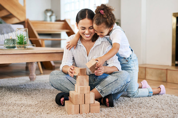 Veamos qué tan alto podemos construir esta torre. una madre y su hija jugando con bloques de madera juntos en casa - Foto, imagen