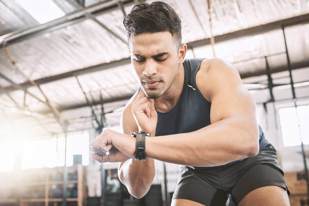 Fit trainer checking his pulse after a workout. Young athlete timing his progress on a watch after exercise. Bodybuilder tracking his heartbeat during a training exercise. Sporty man in the gym. - Zdjęcie, obraz