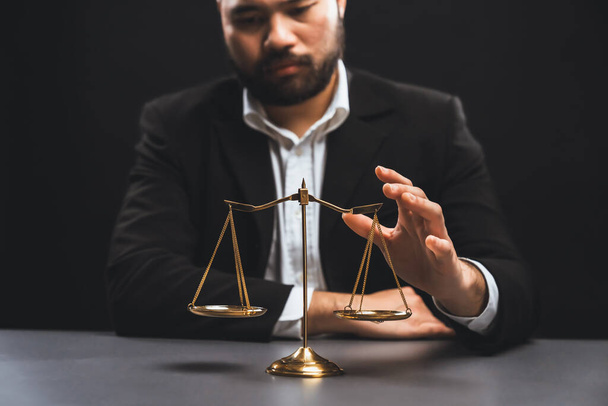 Focus golden scale balance with burred background of lawyer in black suit sit on his office desk, symbol of legal justice and integrity, balanced and ethical decision in court of law equility - 写真・画像