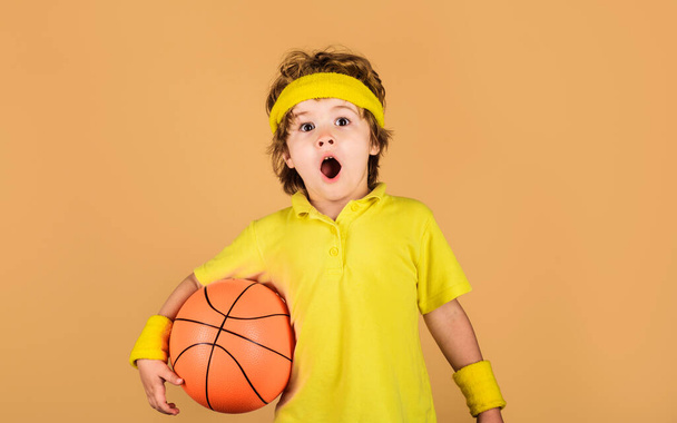 Удивленный мальчик в спортивной форме с баскетбольным мячом. Маленький баскетболист. Спортивный инвентарь Баскетбол. Активный спорт образ жизни. Детство и спорт. Мальчик играет в баскетбол с баскетбольным мячом - Фото, изображение