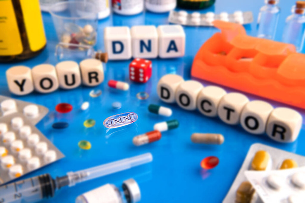 DNA pill on a blue table surrounded by various drugs and a vitamin. Wooden cubes with the inscription YOUR DNA - YOUR DOCTOR. - Photo, image