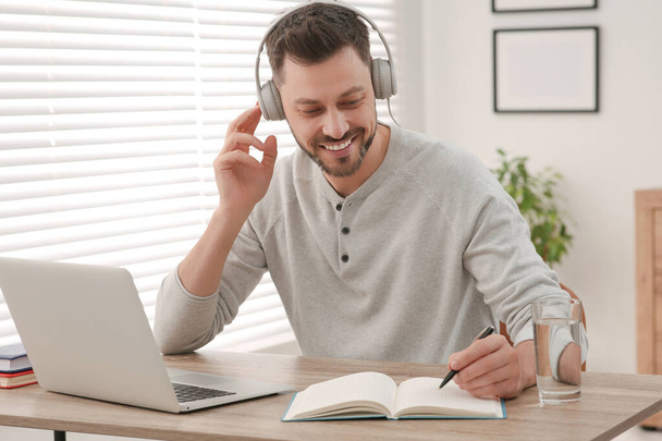 Online translation course. Man in headphones writing near laptop at home - 写真・画像